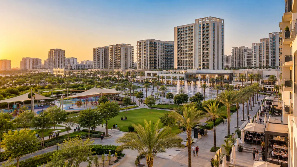 Town Square Dubai’s landscaped community plaza at sunset, featuring modern apartment buildings, palm-lined walkways, green parks, children’s play areas, fountains and outdoor cafés.